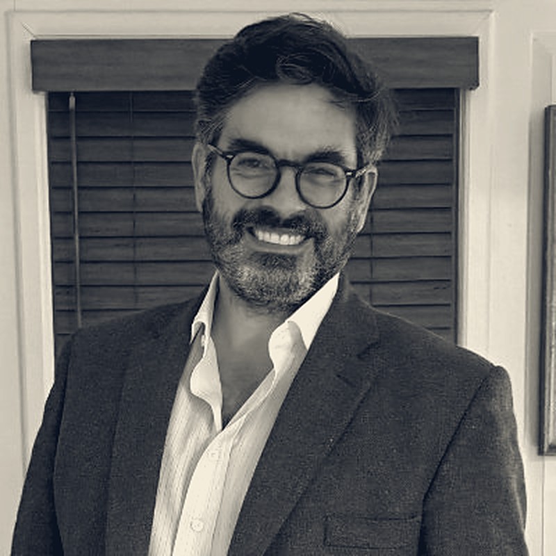 Portrait of Preston Byrne, smiling, in glasses and a tweed jacket.